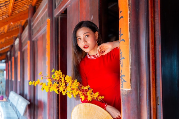 Vietnamese girl with ao dai dress standing in traditional house of vietnam text in photo mean best wishes to family happiness prosperity health tet holiday and new year