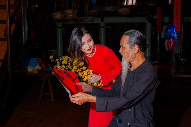 Vietnamese girl with red ao dai dress and old scholars writing calligraphy at lunar new year calligraphy is a popular tradition during tet holiday text in photo mean happy new year and peace