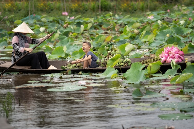 Vietnamese jongen speelt met moeder die op de traditionele houten boot vaart om de roze lotus te houden