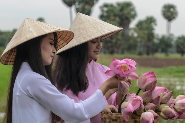 Vietnamese meisjes dragen nationale jurk en opvouwbare lotusbloemen op een fiets.