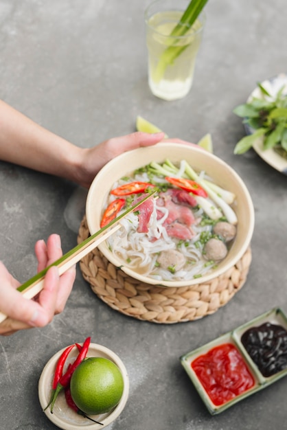 Вьетнамский суп с лапшой фо. Говядина с перцем чили, базиликом, рисовой лапшой и побегами фасоли с изображением лапши, собранной палочками для еды