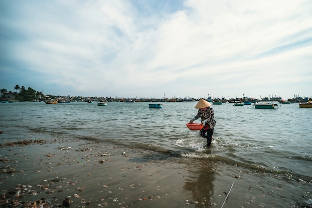 Vietnamese vrouw in een kegelvormige hoed wast schaaldieren in een mand in de zee. MUI nee. Vietnam. 27.01.2019