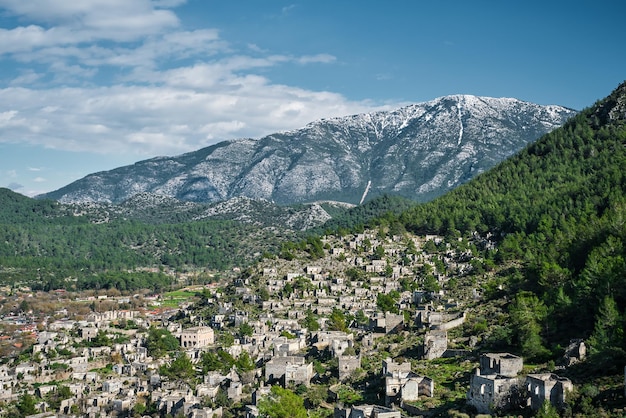 View of an abandoned city near Kayakoy village and snowcapped mountains Abandoned ghost town Karmilisos in winter in Fethiye Turkey ruins of stone houses Site of the ancient Greek city