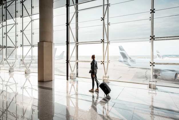 View on the aiport window with woman walking with suitcase at the departure hall of the airport. Wide angle view with copy space