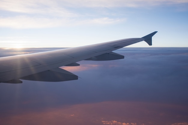 太陽光線と日没の美しい雲の上の飛行機の翼の眺め。旅行と交通