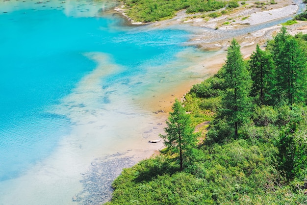 View above on amazing vivid azure mountain lake in valley. Conifer trees in sunlight. Rich vegetation of highlands