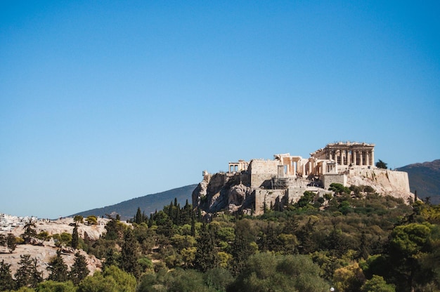 木々のある丘の上の古代アテナイのアクロポリスの眺めギリシャのアテネ