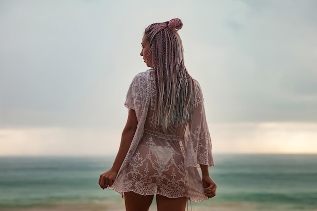 Vista posteriore della giovane donna alla moda con l'acconciatura alla moda sullo sfondo del cielo nuvoloso e del mare