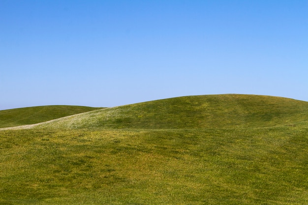 Photo view of bare green hills with a blue sky.