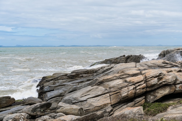 View of the beach of Rio das Ostras in Rio de Janeiro with sunny day, blue sky and some clouds. Strong sea and yellowish sand and lots of rocks.