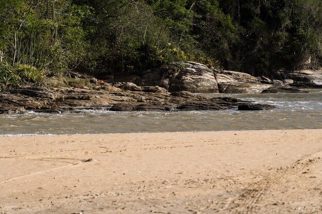 View of the beach of Rio das Ostras with the meeting of the river in Rio de Janeiro. Sunny day, blue sky. Yellow sand and some rocks. Wooden bridge to cross. Boats and fishing on the pier.