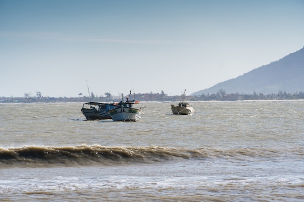 View of the beach of Rio das Ostras with the meeting of the river in Rio de Janeiro. Sunny day, blue sky. Yellow sand and some rocks. Wooden bridge to cross. Boats and fishing on the pier.