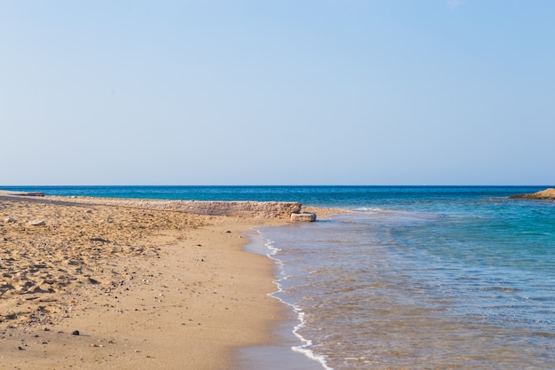 View of beautiful beach with clear blue water, golden sand, colorful boats and mountain. Summer landscape of Greece and Ionian Sea.