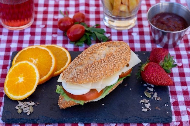 Above view of a black stone cutting board with sesame seed bun with vegetables eggs and cheese Checkered tablecloth red wine glass