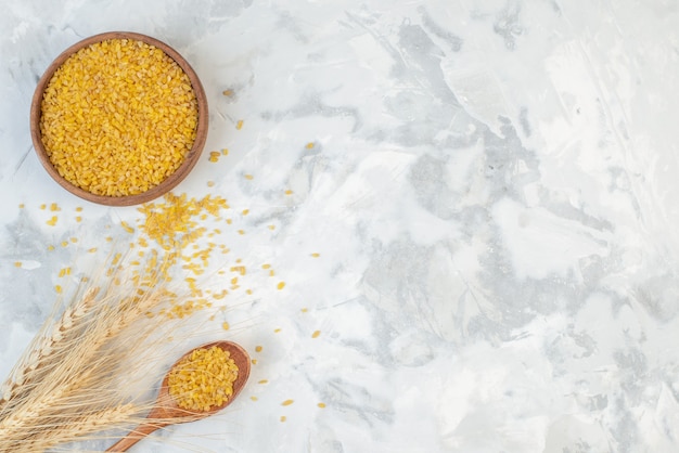 Above view of brown rice in a brown bowl spikes on the left side on ice background with free space