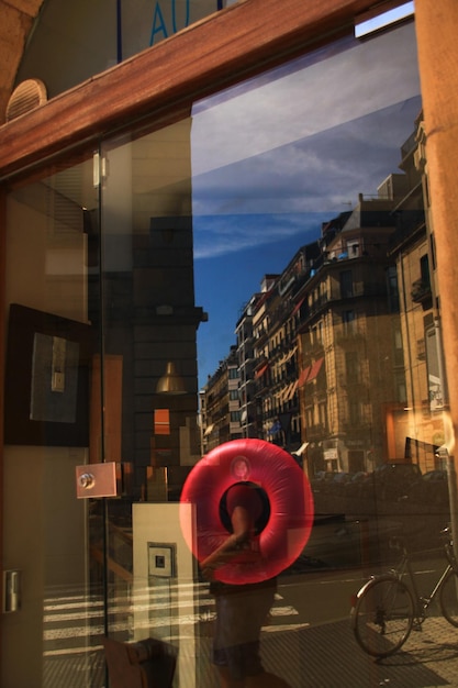 View of building and a man carrying pink globe reflected in a glass mirror of a shop