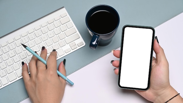 Above view businesswoman holding mobile phone and typing on wireless keyboard