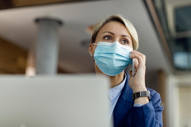 Below view of businesswoman with face mask talking on mobile phone