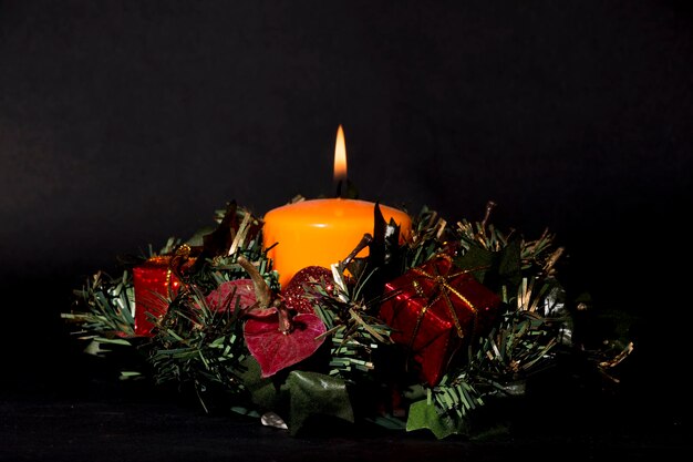 View of a Christmas centerpiece which has an orange candle burning Everything stands out on a black background