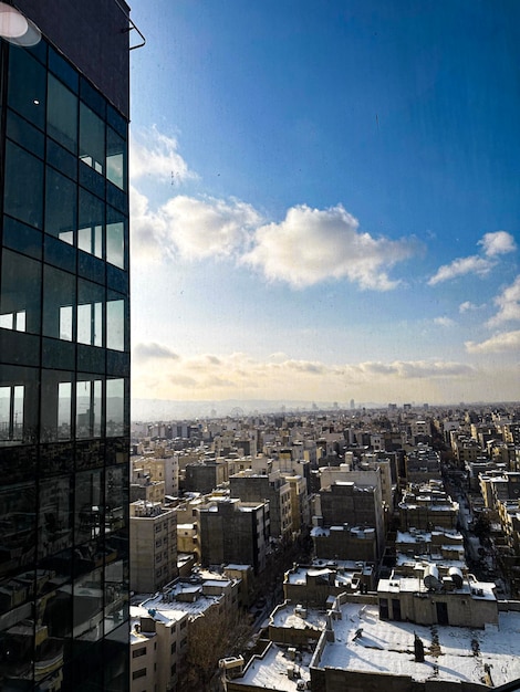 A view of a city from a window in a building with a blue sky and clouds.