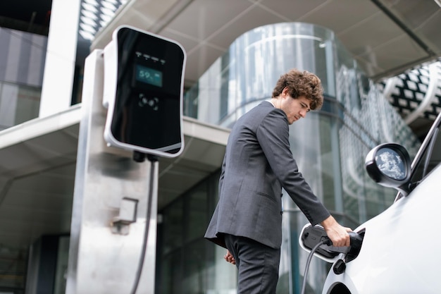 以下のビューのクローズ アップ プログレッシブ ブラック スーツのビジネスマンは、EV 車のバッテリーを充電します。