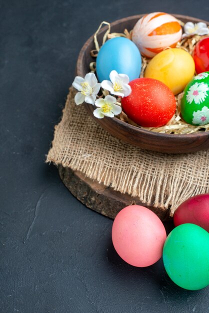 above view colored easter eggs inside plate with straw on dark surface