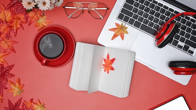 Above view computer laptop notebook headphone and coffee cup on red background with maple leaves