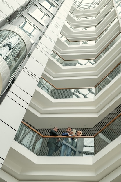 Below view of concentrated business people standing at railing and analyzing online document on tablet in modern office center