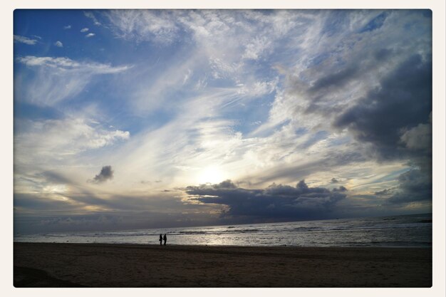 View of couple on beach against cloudy sky