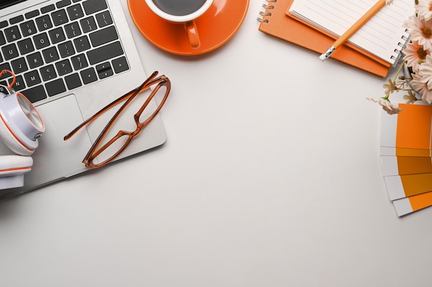 Above view of creative workspace with laptop computer headphone\
glasses coffee cup and notebook on white table