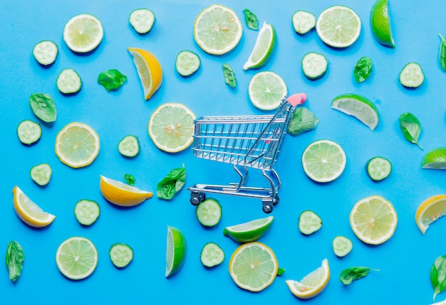 Above view at cutted lemons and limes and shopping cart on blue background