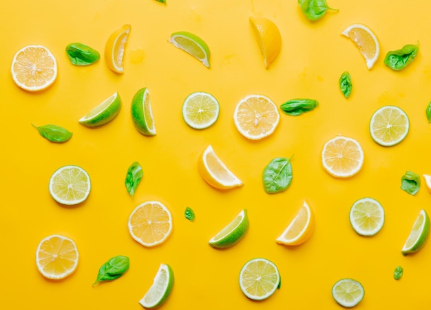 Above view at cutted lemons and limes with cucumbers on yellow background