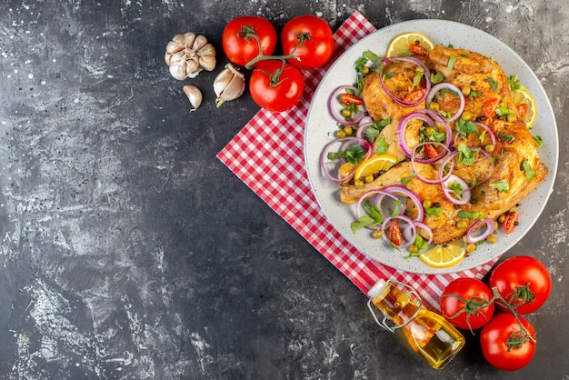 Above view of delicious dinner fried chicken dish with various spices and foods tomatoes with stems garlics fallen oil bottle lemon on the left side on dark color background