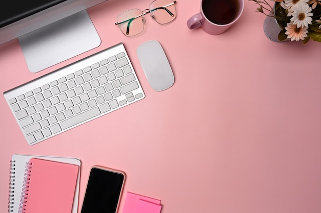 Above view designer workspace with, smart phone, glasses and notebook on pink background.