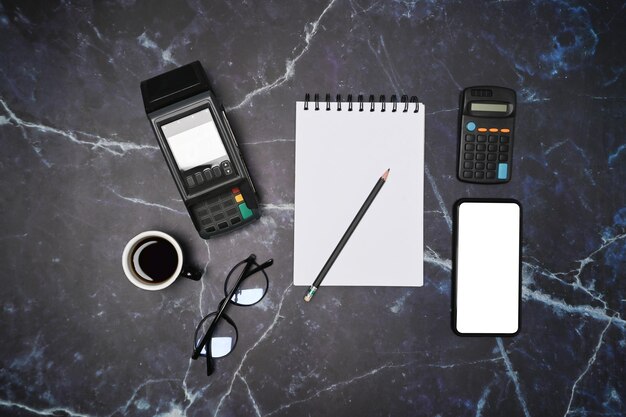 Above view empty notepad glasses coffee cup smart phone and payment terminal on marble background