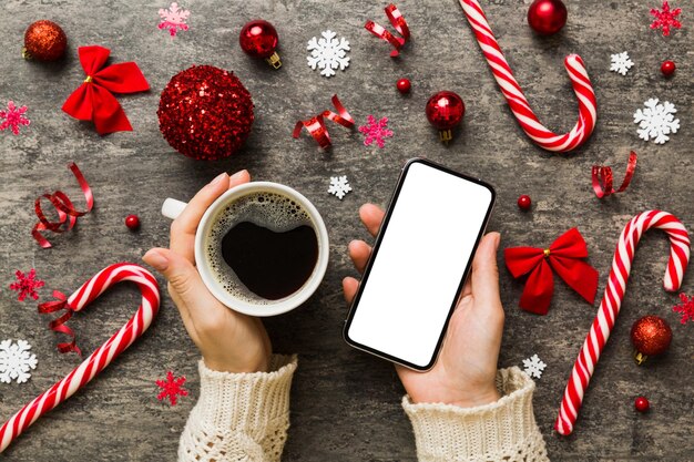 Photo above view of female hand holding smart phone with hot cup of coffee christmas decoration on colored background