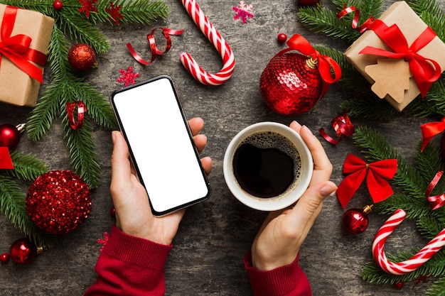 色付きの背景にホット コーヒーのクリスマスの装飾とスマート フォンを持っている女性の手の上のビュー