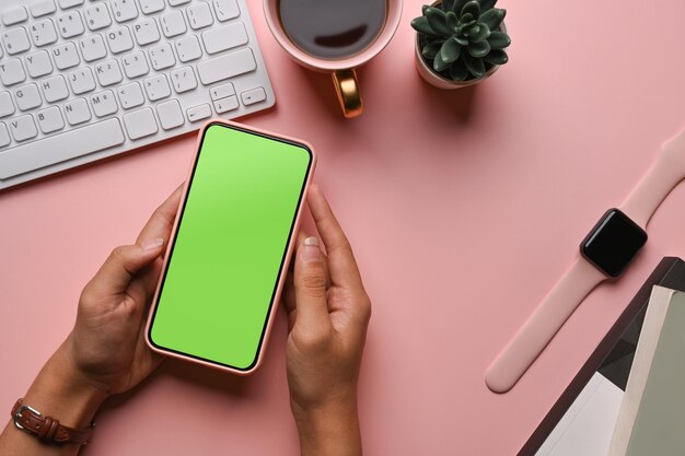 Above view of female hands holding mock up mobile phone on pink pastel background.