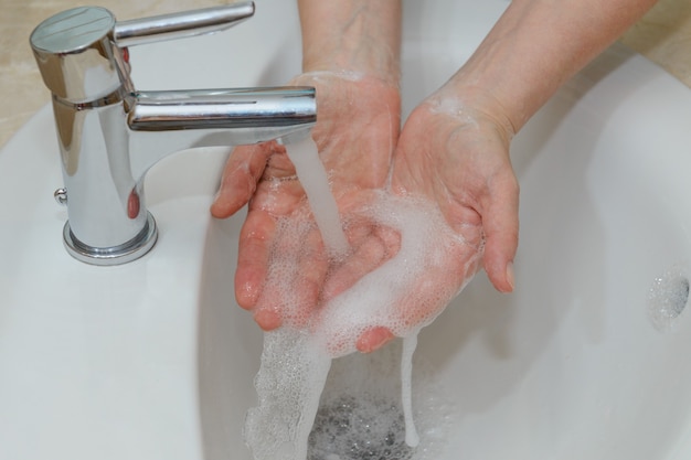 Vista delle mani femminili in schiuma saponosa sotto il primo piano dell'acqua di rubinetto