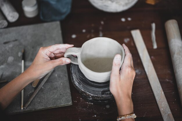 View of female hands works with clay makes future ceramic plate\
ceramic artist makes classes of hand building in modern pottery\
workshop creative people handcrafted design