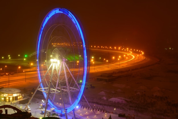 Вид на карусель колеса обозрения с синей подсветкой ночью зимой