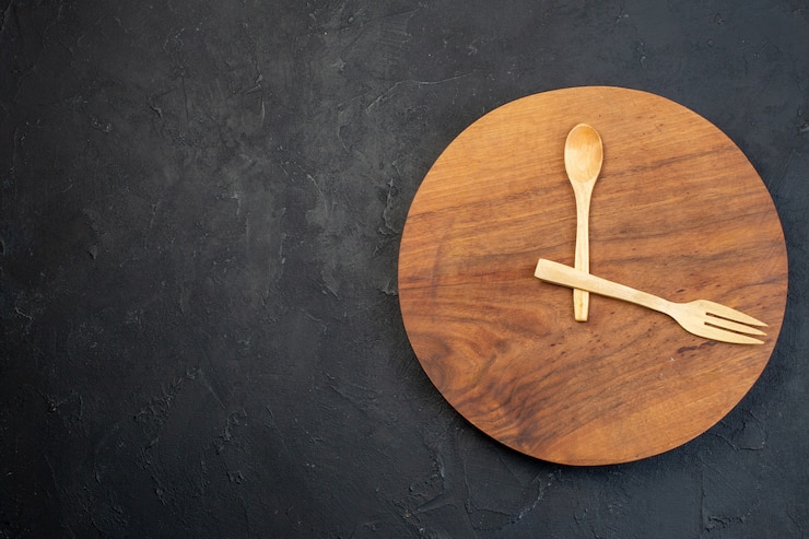 Above view of fork and knife empty brown round cutting board on the left side on black background with free space