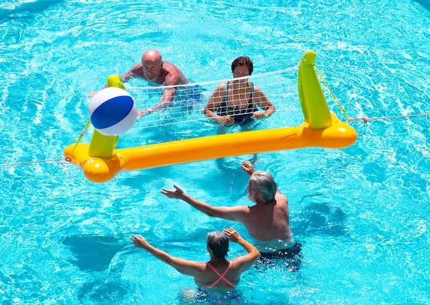 Sopra la vista di quattro persone anziane che giocano a pallavolo nell'acqua della piscina estate e vacanza