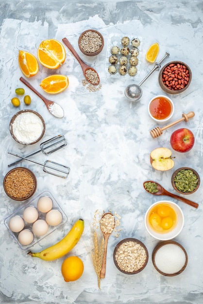 Above view of free space flour in a bow cracked eggs fresh fruits raw oatmeal on ice background
