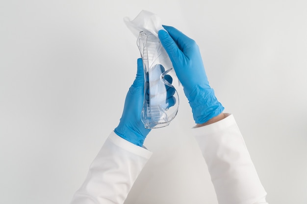 Фото Вид сверху медсестра в синих латексных перчатках на белой стене обрабатывает пластиковые очки, чтобы защитить пациентов от больных.