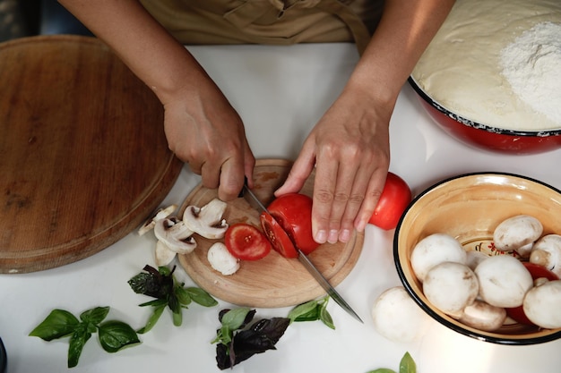 사진 위에서 보기 요리사는 도마에 토마토를 자르고 식탁에 얇게 썬 샴피뇽과 허브를 올려 놓습니다.