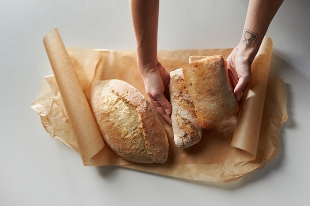 Фото Вид сверху человеческих рук, кладущих свежий хлеб на бумагу для выпечки