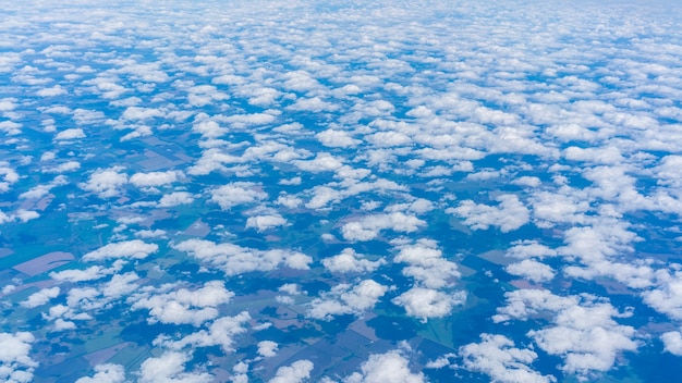 Вид из окна самолета: небольшие группы облаков, рассеянные и плывущие в голубом небе, как хлопок, над землей России, покрытые тенью облаков в некоторых частях ландшафта.