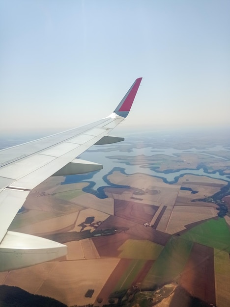 View from airplane window with wing above agricultural field and dam