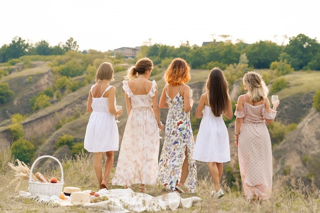 Photo view from back. the company of gorgeous female friends enjoys a summer green hlls landscape and drink alcohol. people concept.